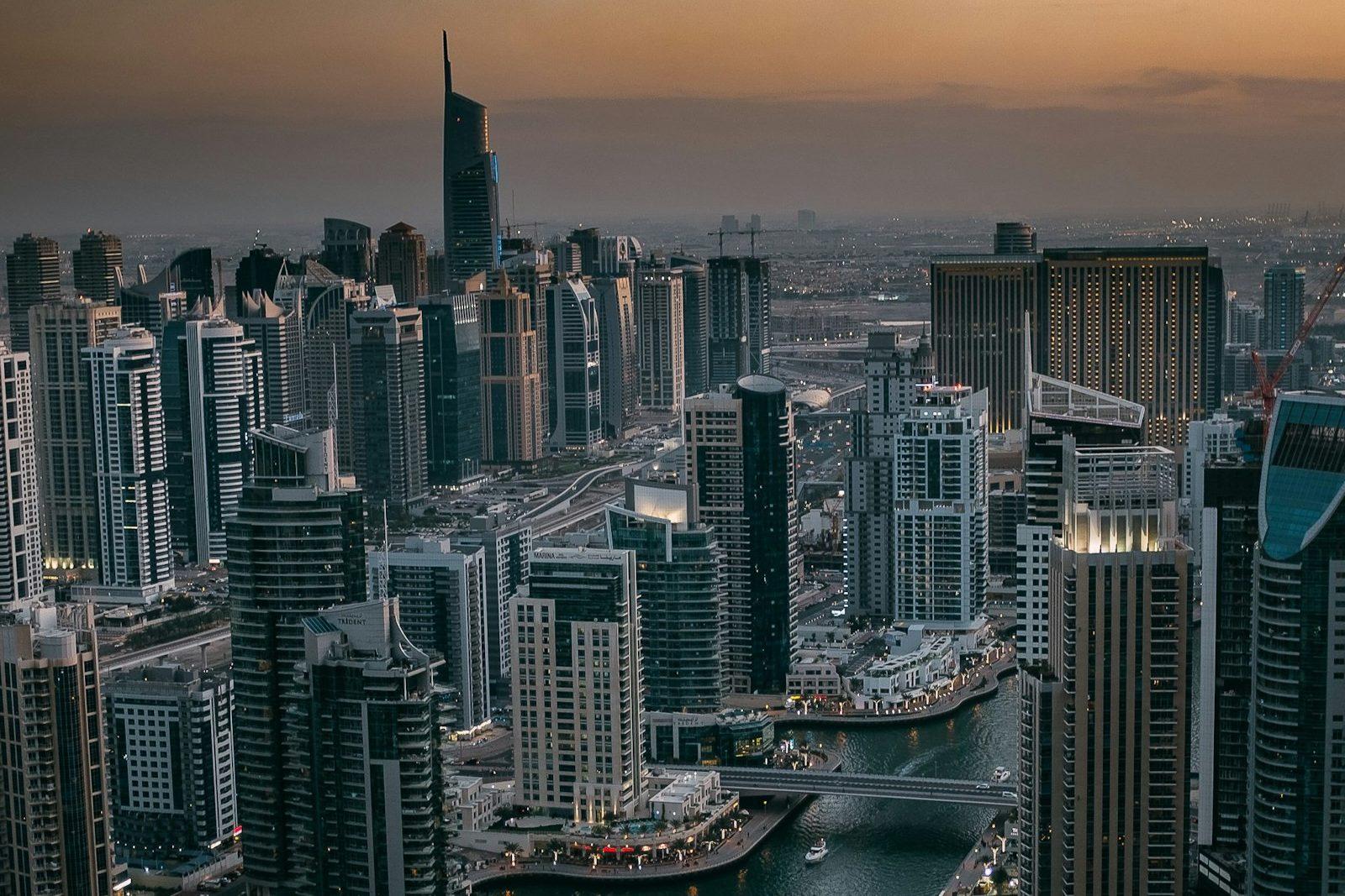 Aerial view over Dubai Marina at dusk, towers packed along both banks of the canal with yachts moored in the channel below.