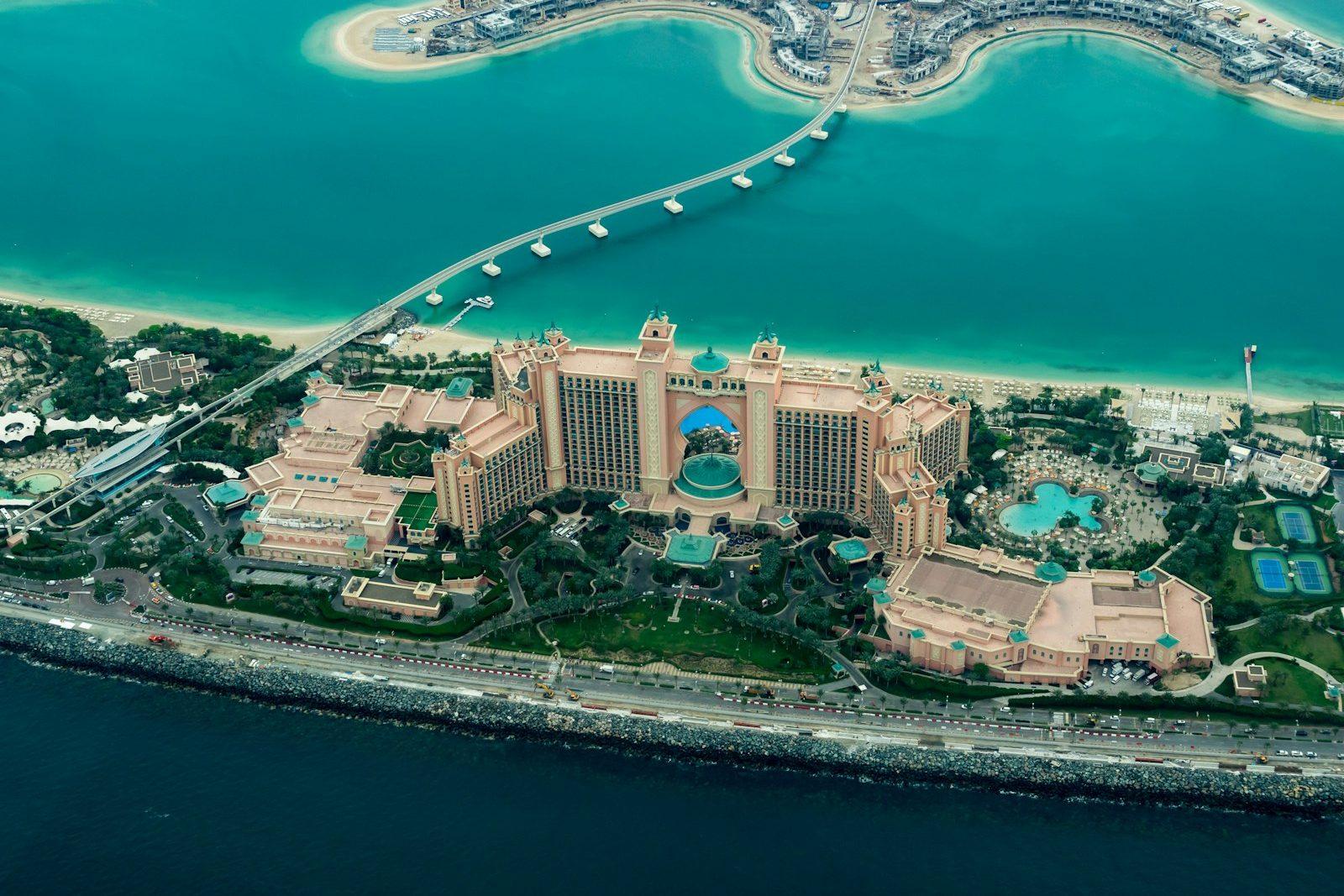 Aerial view of the Palm Jumeirah crescent, the Atlantis resort at its centre ringed by turquoise shallows and the monorail causeway.