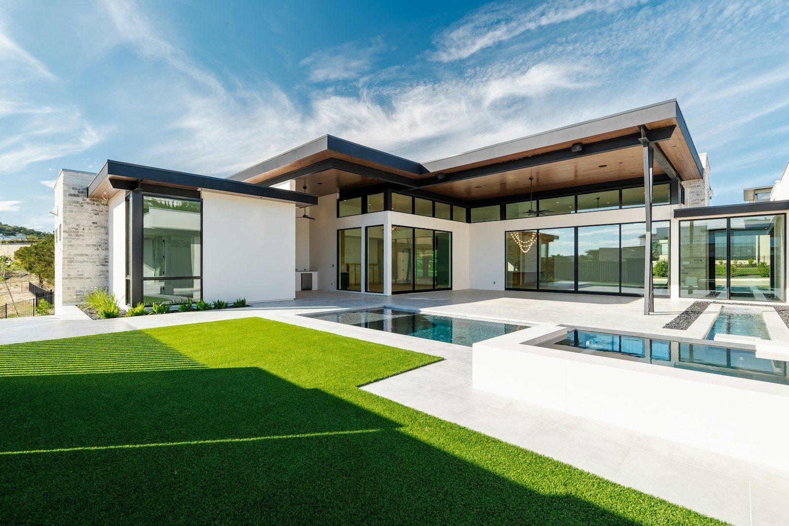 Rear elevation of a contemporary villa: a flat-roofed, timber-soffited pavilion with full-height glazing opening onto a lawn and a rectangular pool.