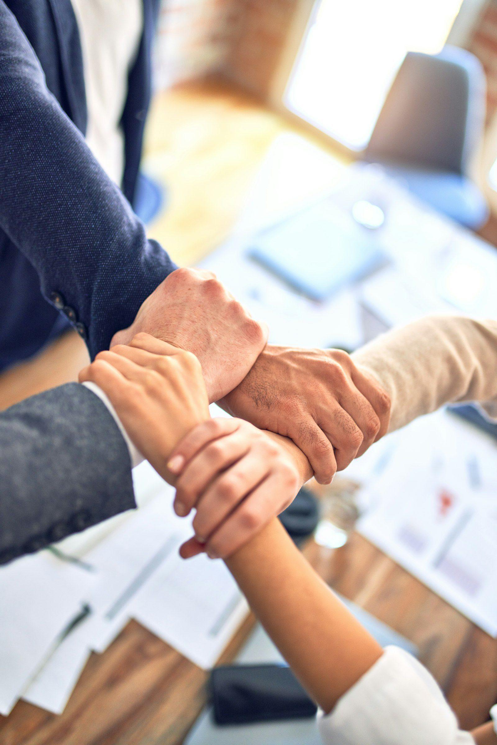 Overhead view of two people clasping hands across a desk scattered with printed documents.