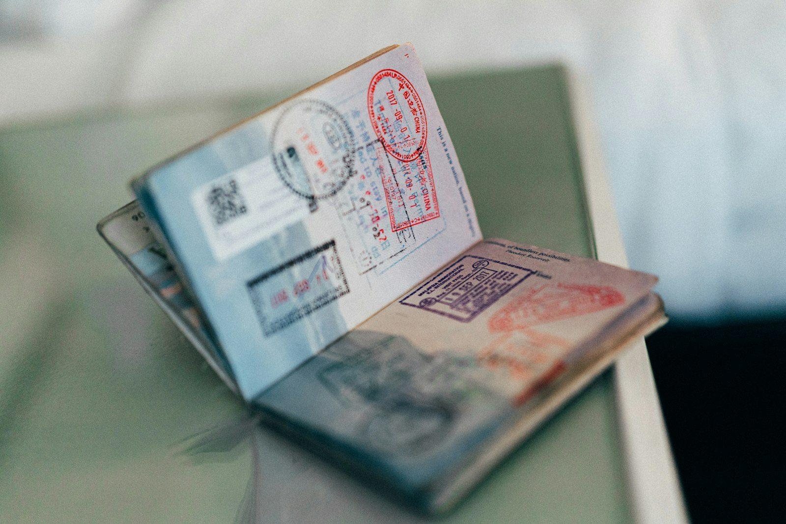 An open passport standing on a desk, its visa pages showing entry stamps and a residence sticker.
