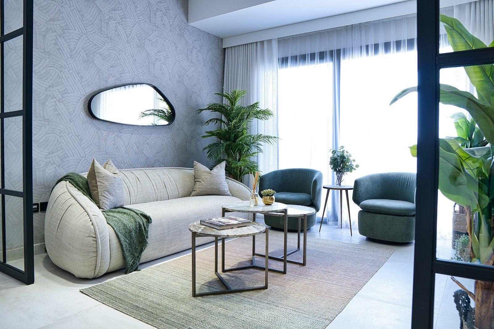 Living room with a deep bouclé sofa, two green velvet swivel chairs, marble side tables and a black steel-framed screen dividing the reception from the hall.