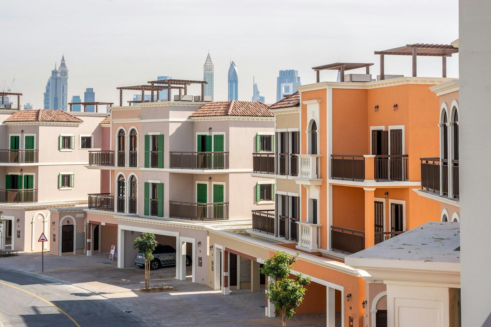 Townhouse street with covered parking bays and shuttered balconies, the towers of Sheikh Zayed Road standing behind the roofline.