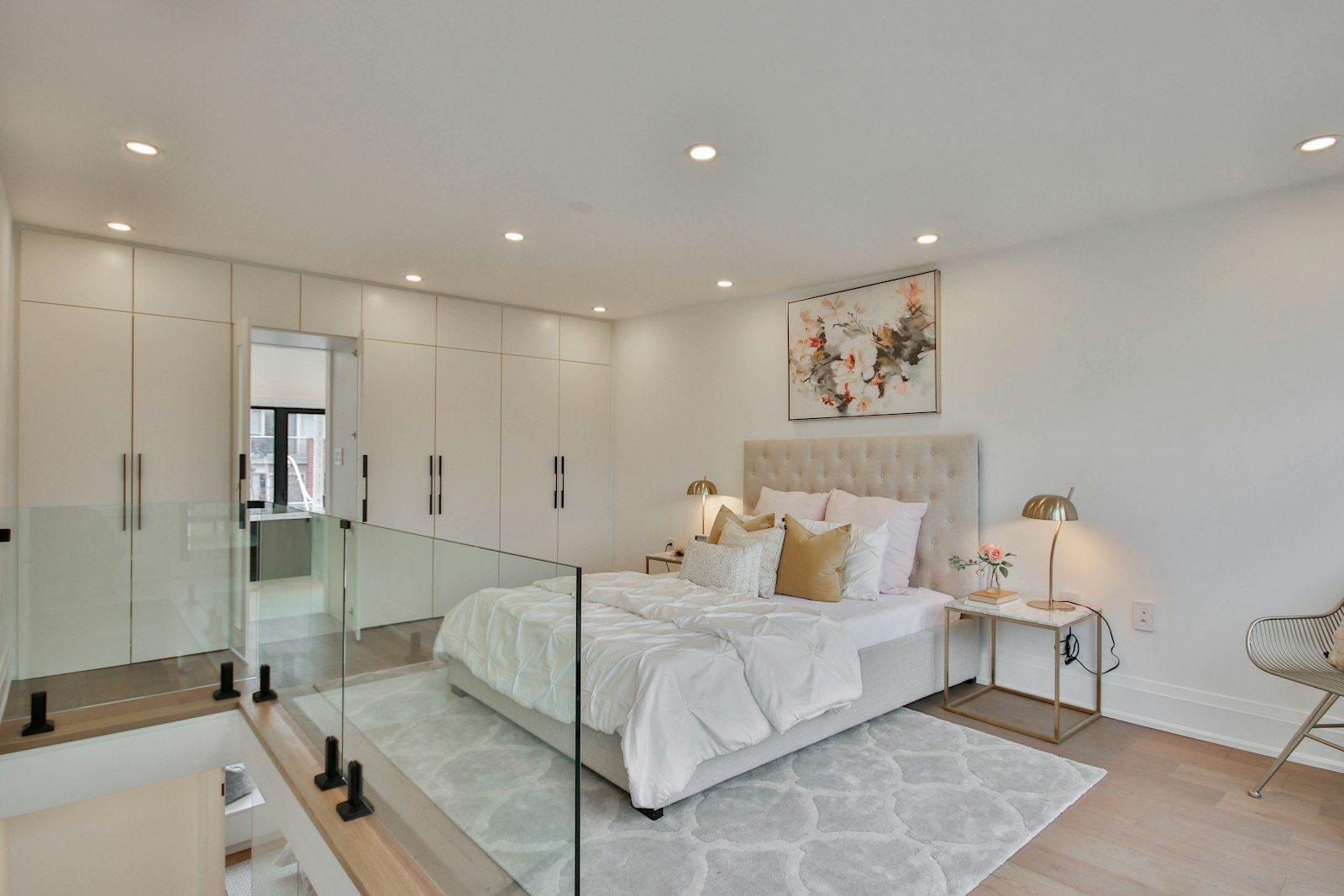 Principal bedroom with a run of fitted wardrobes along one wall, an upholstered bed and a glass-balustraded stair landing at the edge of the room.