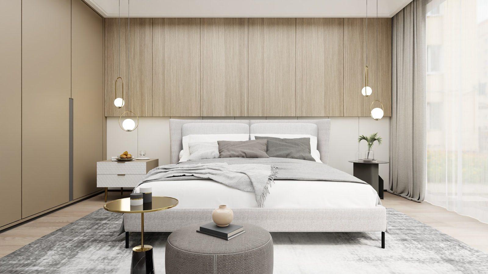 Furnished bedroom in a contemporary show interior: a fluted oak headboard wall, pale grey upholstered bed, brass ring pendants either side, full-height wardrobes and sheer curtains across a tall window.